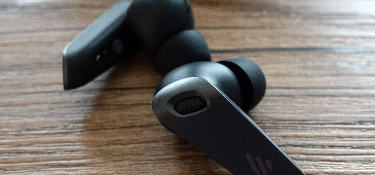 Edifier NeoBuds Plus True-Wireless-Ohrhörer in Schwarz mit Silikon-Aufsätzen auf Holztisch, Nahaufnahme.