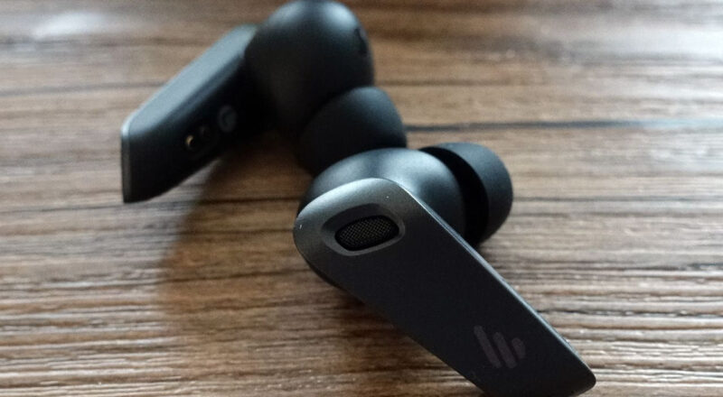 Edifier NeoBuds Plus True-Wireless-Ohrhörer in Schwarz mit Silikon-Aufsätzen auf Holztisch, Nahaufnahme.