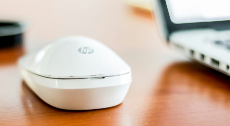 Weiße HP-Maus auf einem Holztisch neben einem Laptop