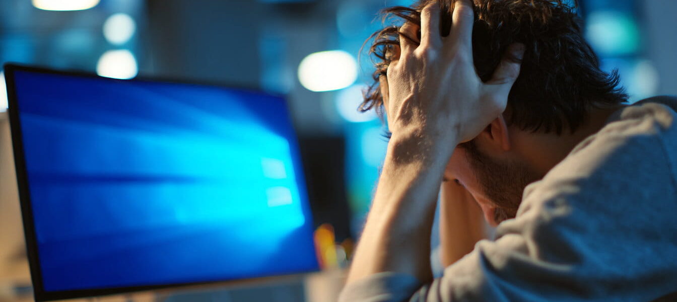 Frustrierter Windows-Nutzer sitzt vor einem PC mit angedeutetem Systemfehler