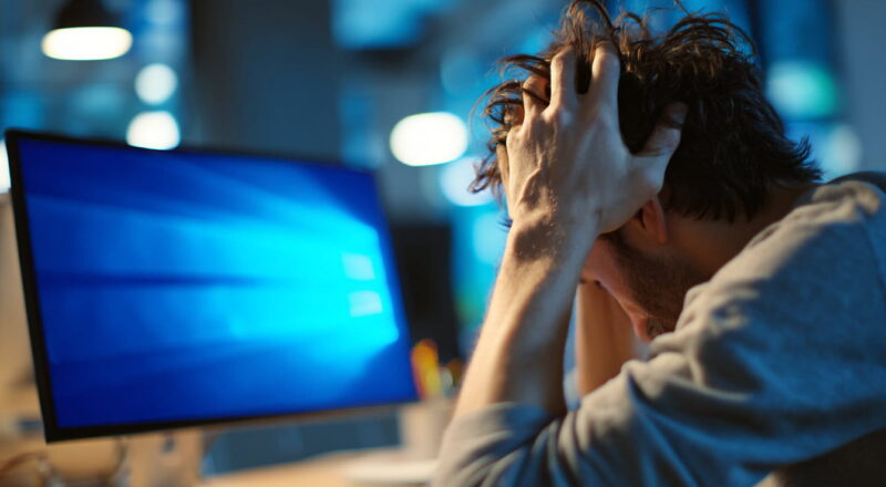 Frustrierter Windows-Nutzer sitzt vor einem PC mit angedeutetem Systemfehler