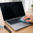 Laptop wird mit Mikrofasertuch gereinigt, daneben liegen Pinsel und Blasebalg als Reinigungszubehör